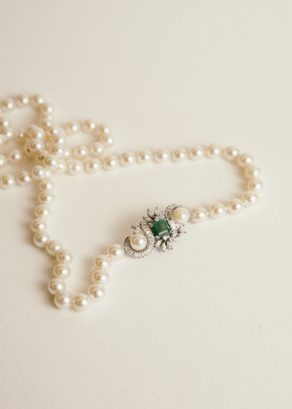 Collar largo de perlas con cierre de metal blanco, piedra verde rectangular en el centro, dos perlas y piedras blancas en talla baguette y marquesa